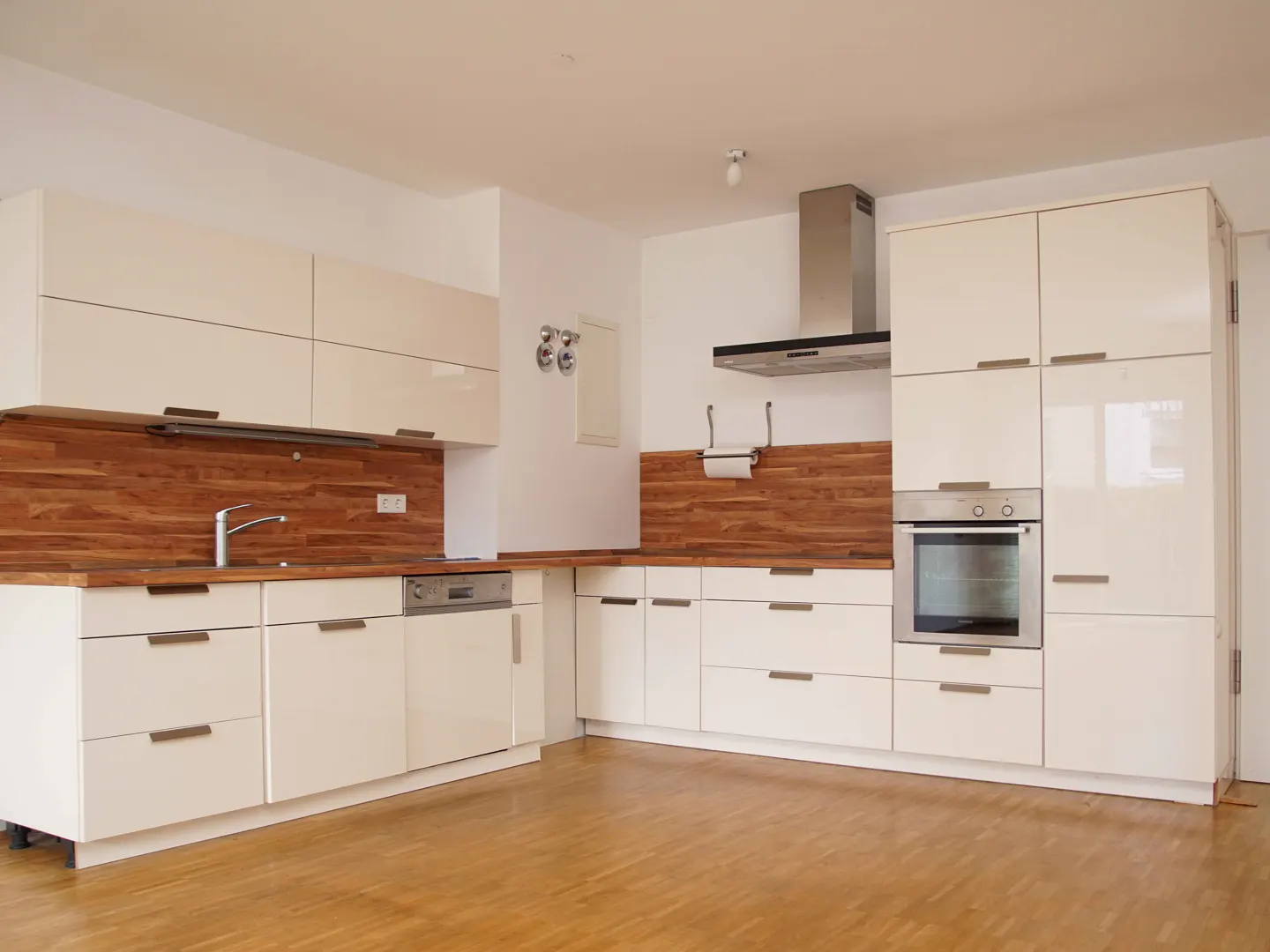 Bright kitchen with white cabinets, wood countertops and backsplash, stainless steel oven and range hood, and wood floor.