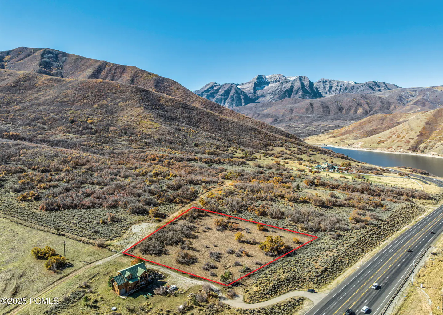 Aerial view of a vacant lot outlined in red, with mountains, a lake, and a highway in the background.