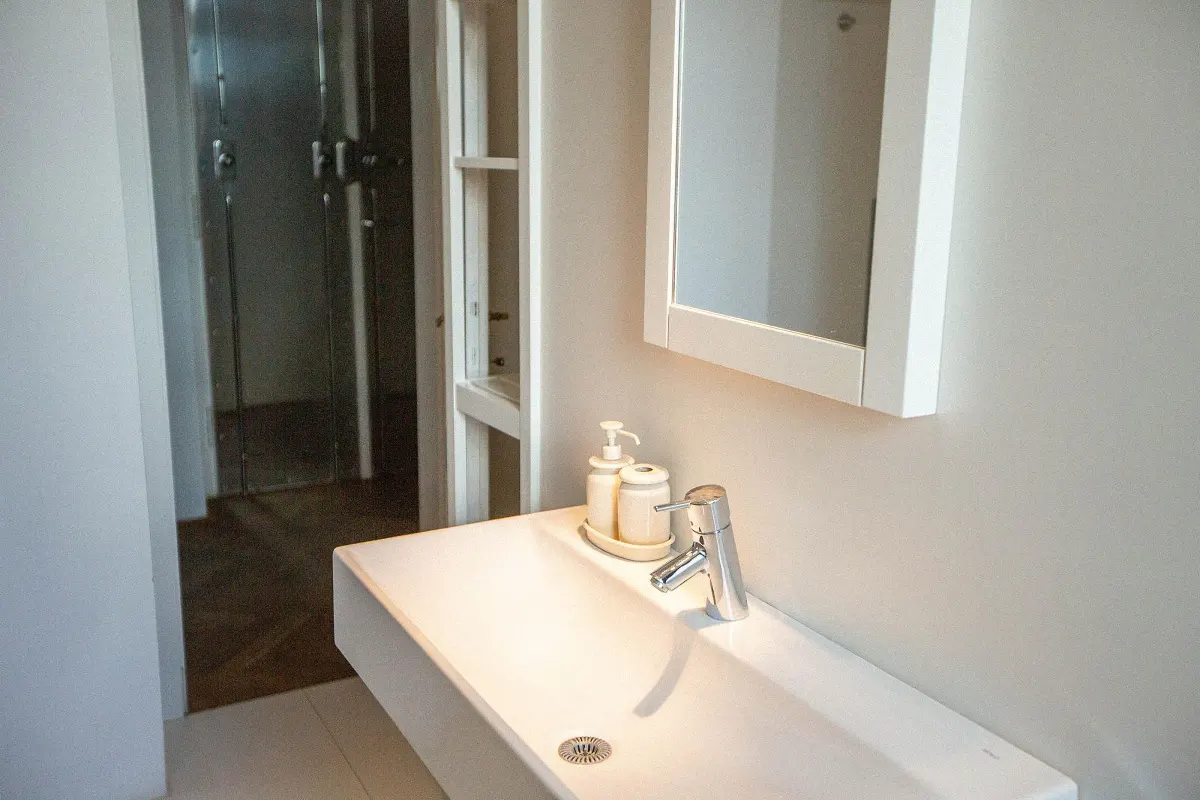 Bathroom with a white rectangular sink, chrome faucet, soap dispenser, and a white framed mirror on a light gray wall.