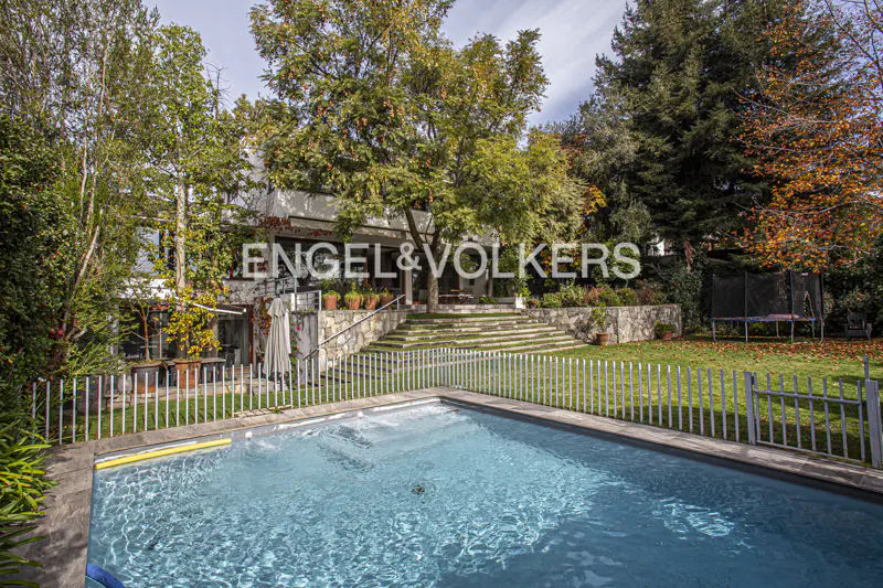 A backyard with a pool, a white fence, and a house with stone steps leading up to it. The Engel & Volkers logo is visible.