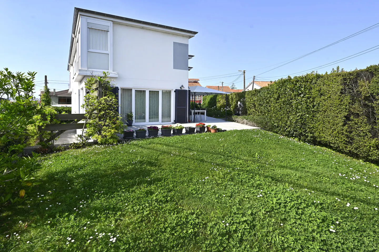 A white two-story house with a green lawn and a patio with a white canopy.