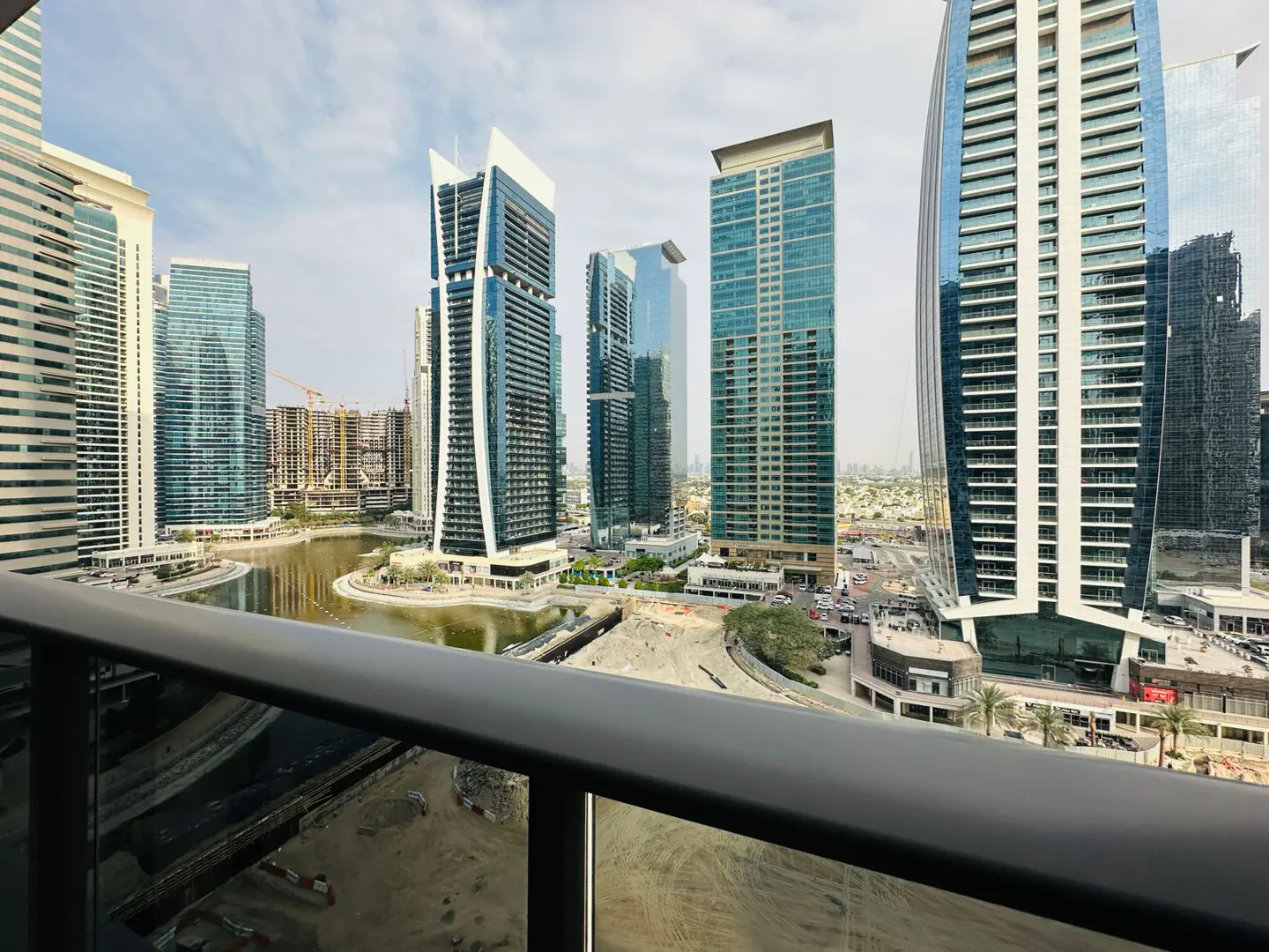 View from a balcony overlooking a Dubai cityscape with modern glass skyscrapers and a winding waterway.