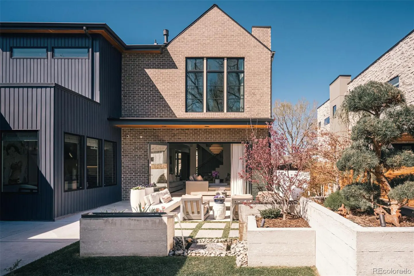 Backyard view of a modern home with a brick facade, open patio doors, and a landscaped garden with concrete planters.