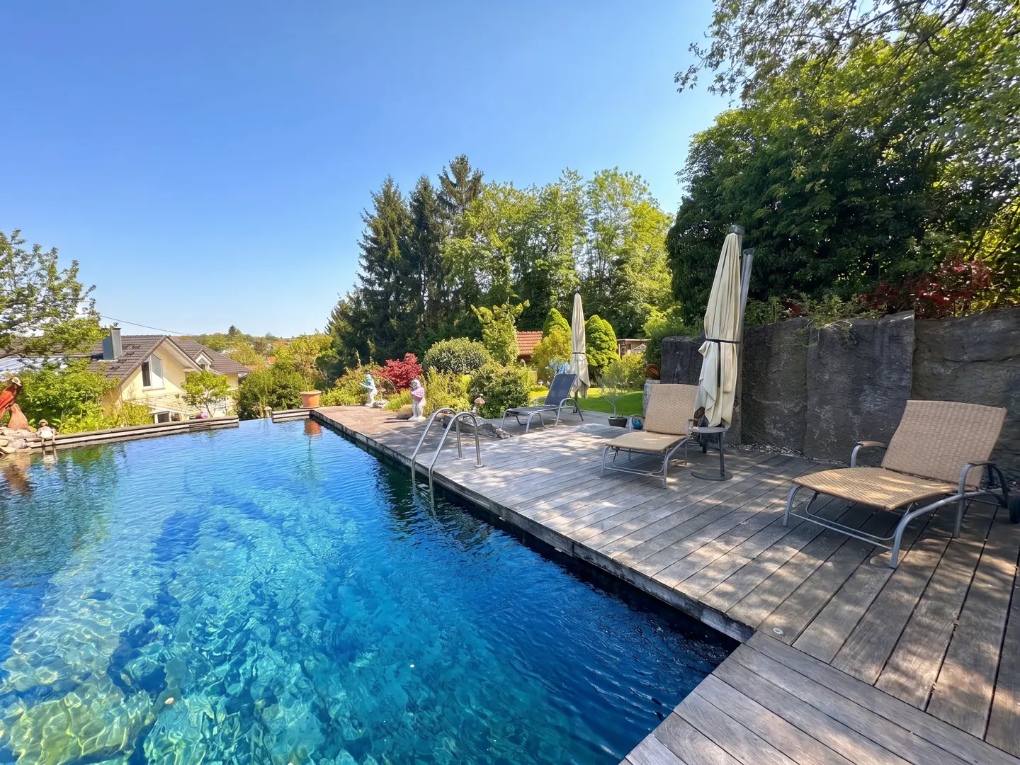 A backyard pool with clear blue water and a wooden deck with lounge chairs under a sunny sky.