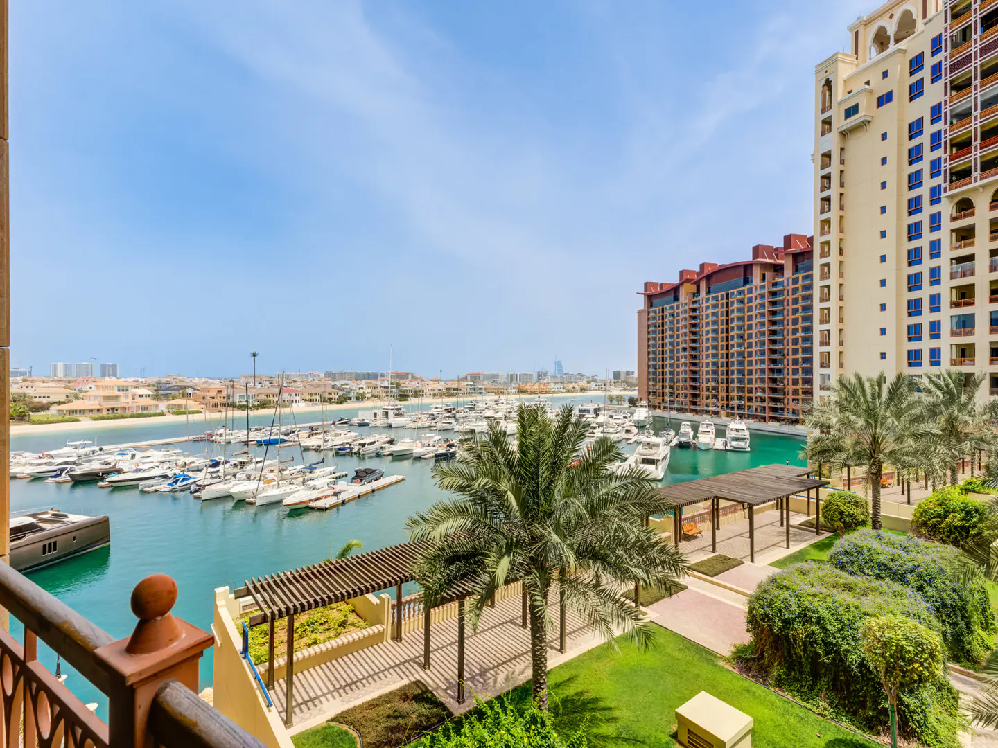 View from a balcony overlooking a marina filled with boats, with tall buildings and palm trees in the background.