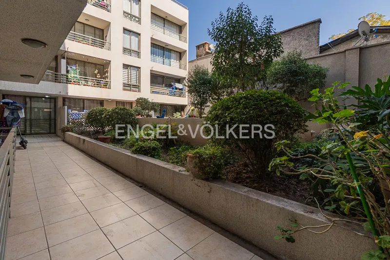 Exterior view of a building with a tiled walkway and garden area. The Engel & Völkers logo is superimposed on the image.