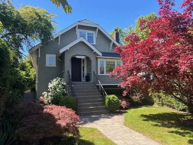 A two-story gray house with a dark front door, steps leading up to it, and a red Japanese maple tree in the yard.