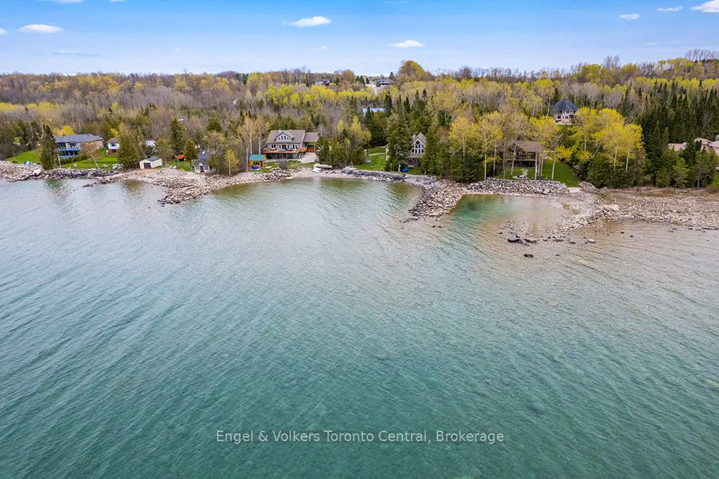 Aerial view of lakefront homes with rocky shoreline and turquoise water under a blue sky.