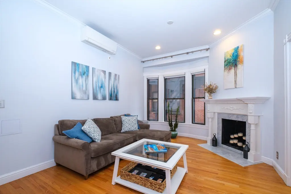 Living room with hardwood floors, a brown sectional sofa, a white coffee table, and a fireplace with a white mantel.