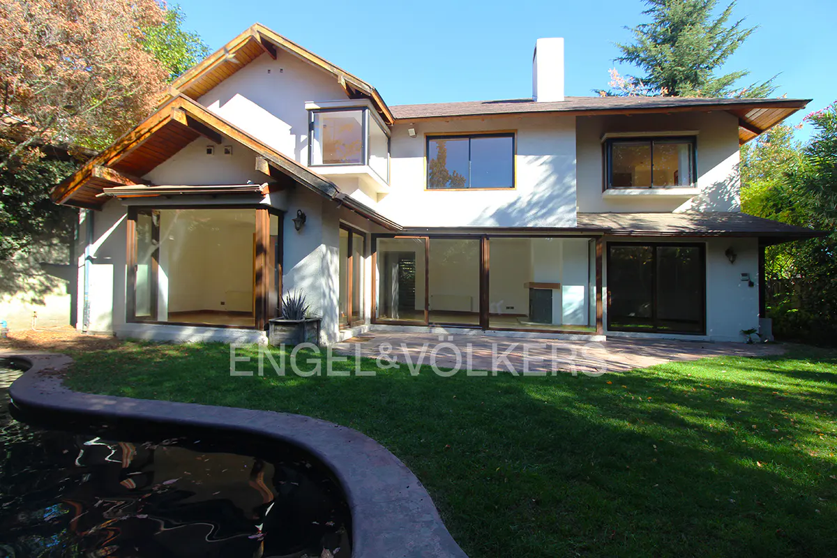 Exterior view of a two-story white house with large windows, a pool, and green lawn. Engel & Völkers logo is visible.