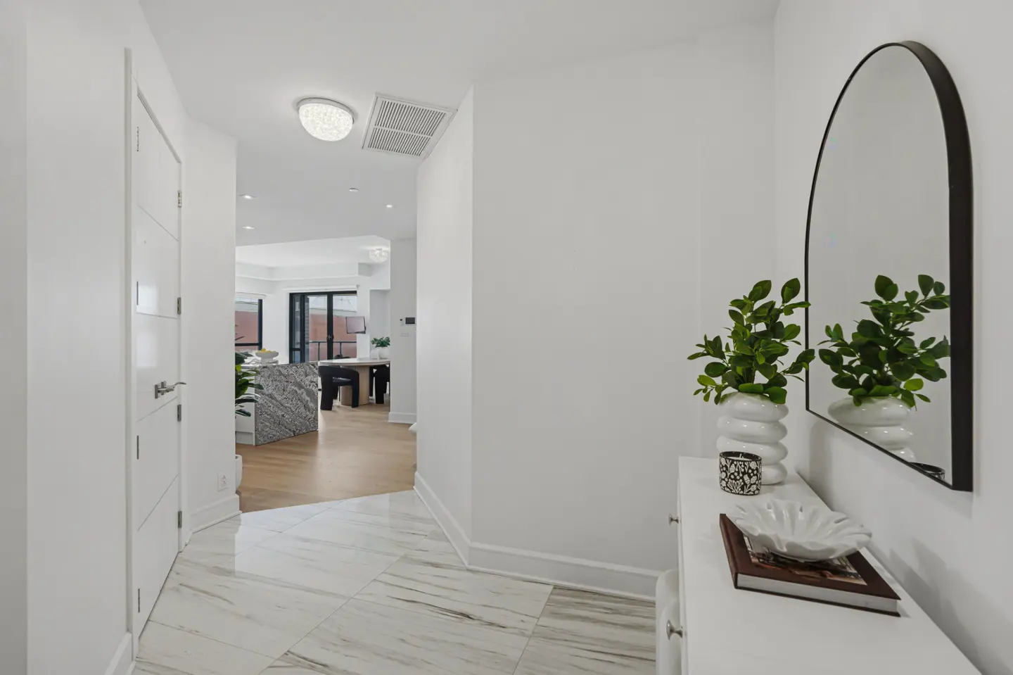 Bright foyer with marble floors, white walls, and a black-framed arched mirror above a white console table with decorative items.