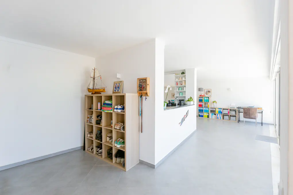 Bright, modern home interior with white walls, gray floors, and a light wood shoe rack filled with shoes and topped with a sailboat model.