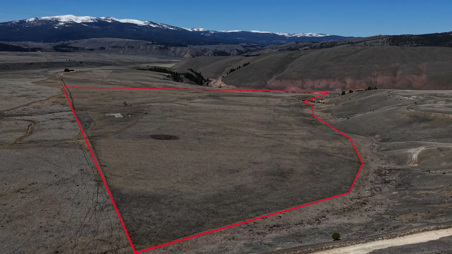 Aerial view of a large, brown, grassy property outlined in red, with mountains and snow-capped peaks in the background.