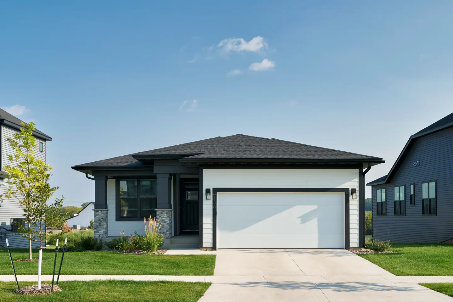 A modern, single-story home with a white garage door, gray accents, and a dark roof under a blue sky.