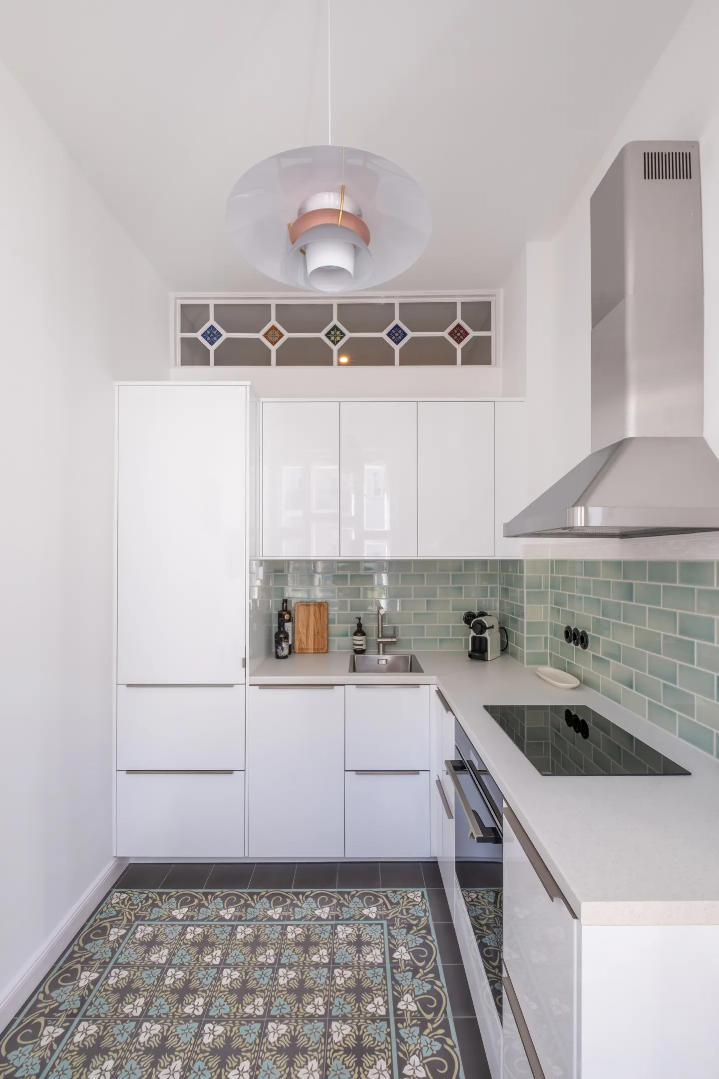 A modern kitchen with white cabinets, light green backsplash, and patterned floor tiles. A stainless steel range hood is visible.