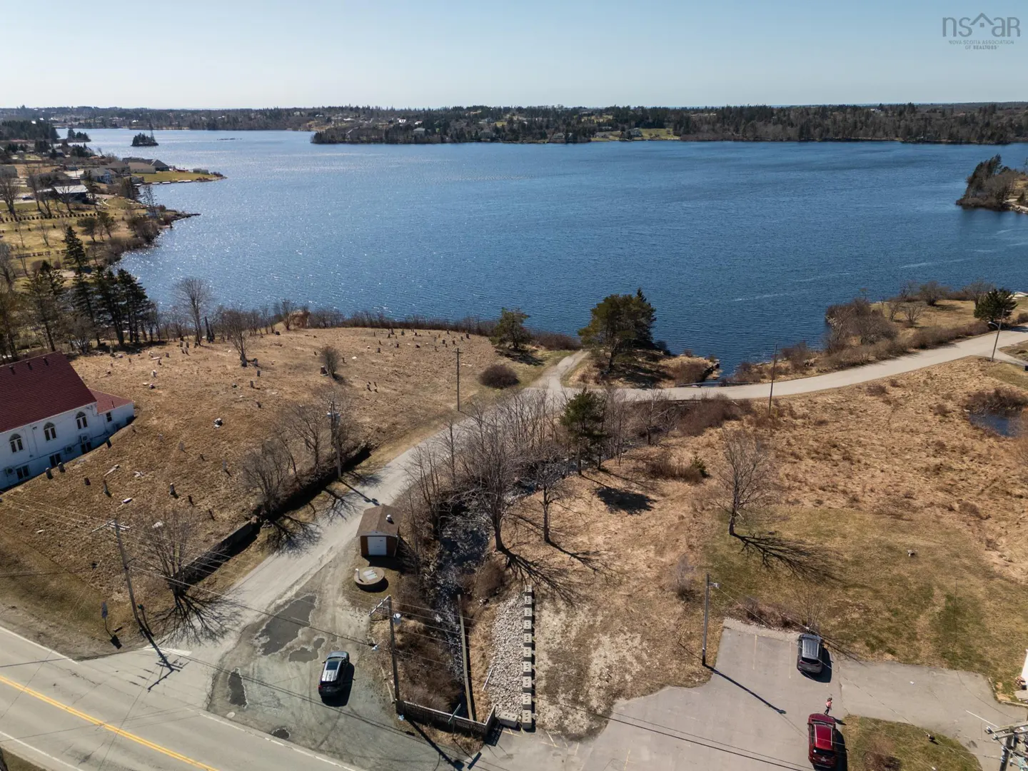 Aerial view of a waterfront property with a building, parking lot, and a road leading to the water.