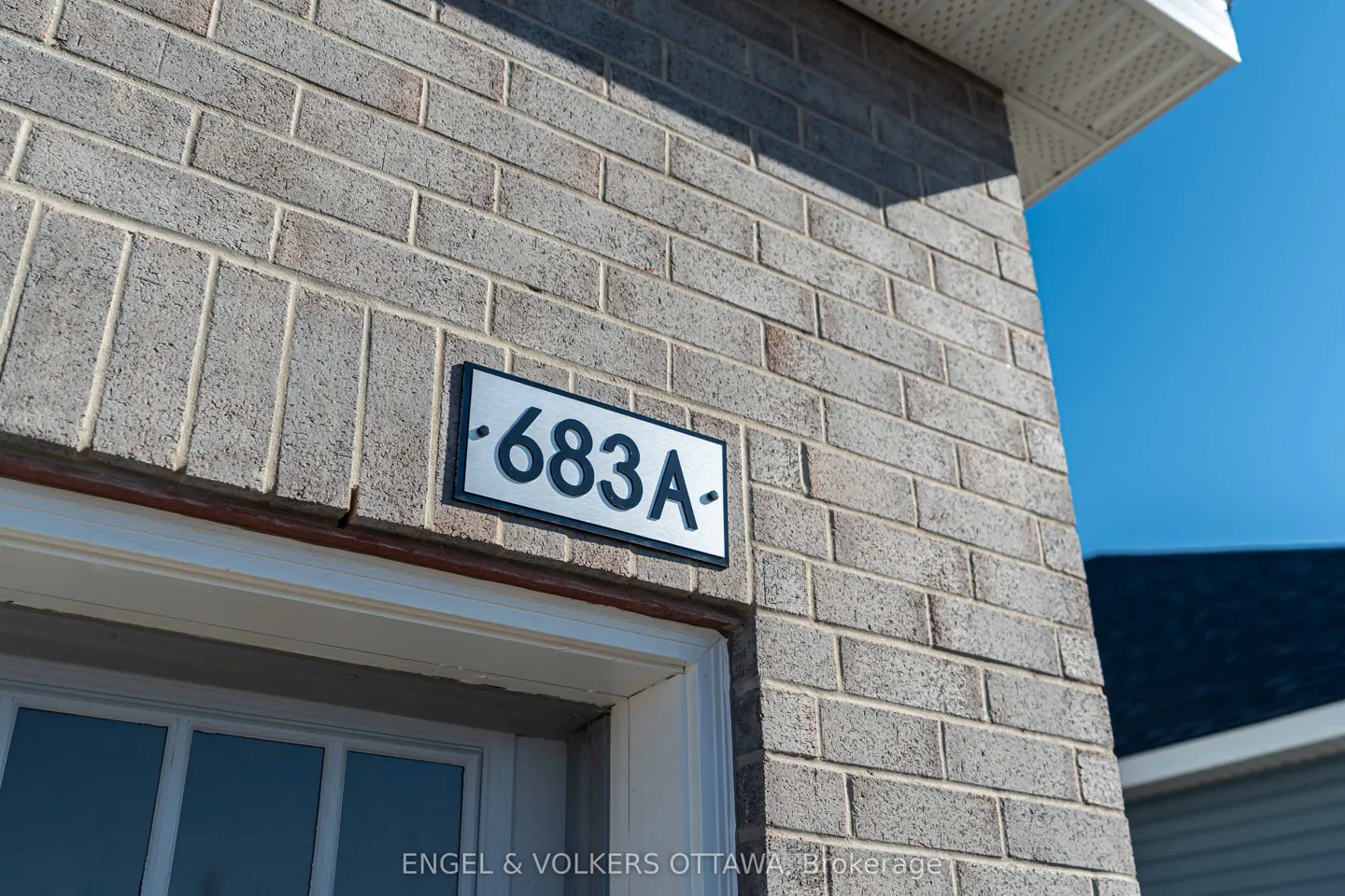 Close-up of a brick building with the address "683A" displayed on a silver and black sign. A white door frame is visible below.