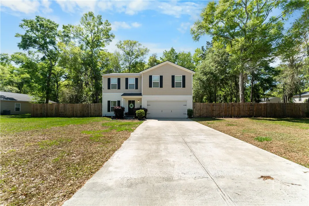 Two-story house with beige and white siding, black shutters, and a two-car garage. A long driveway leads to the house. Trees surround the property.