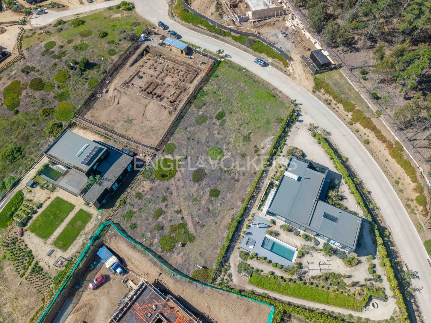 Aerial view of a vacant lot with construction nearby, modern homes, and a winding road. The Engel & Volkers logo is visible.