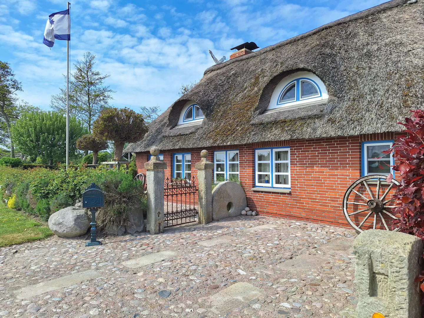 Exterior of a red brick house with a thatched roof and blue-trimmed windows. A flag waves in the background.