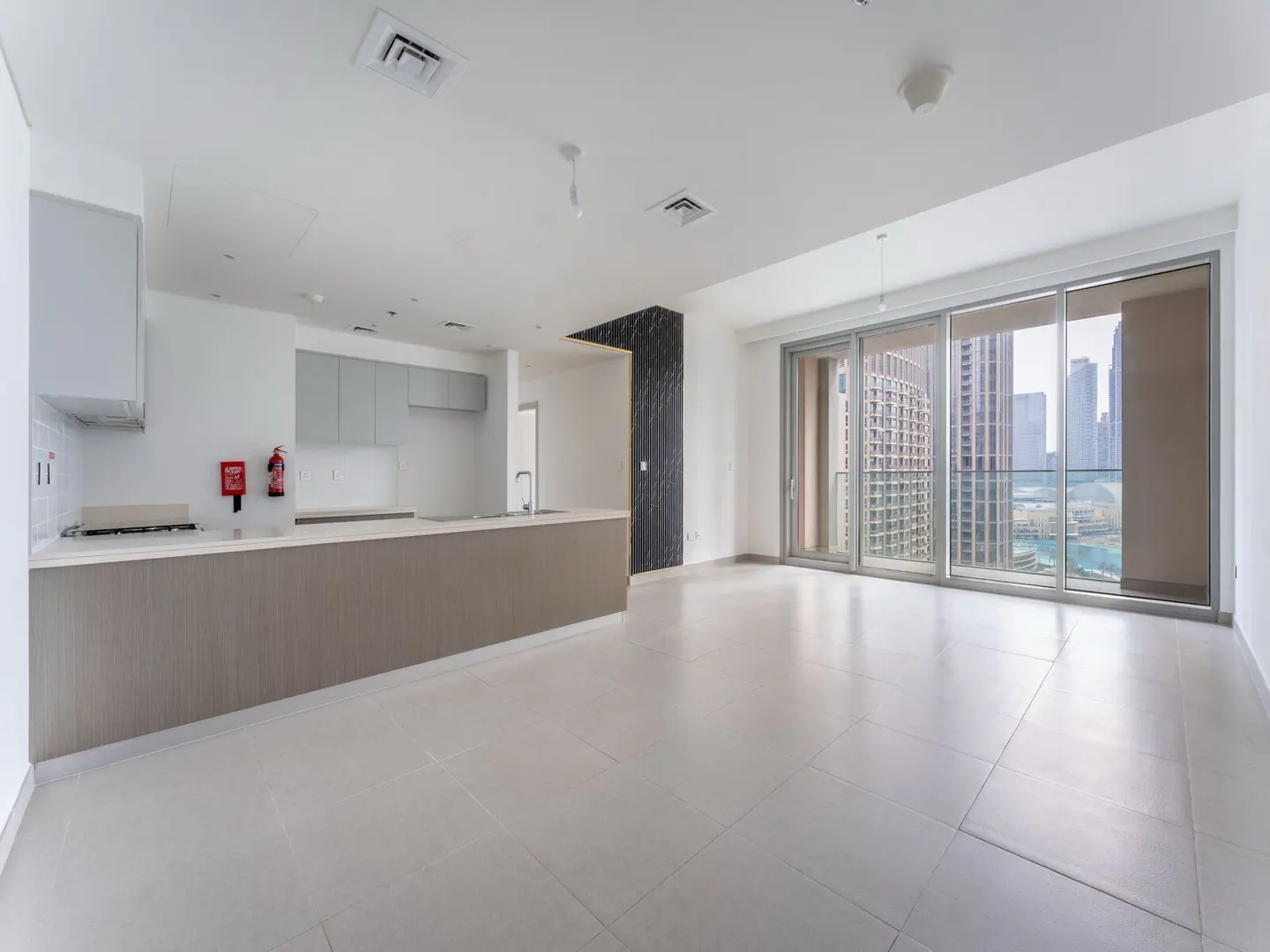 Modern open-plan apartment with a grey kitchen island, white walls, and floor-to-ceiling windows overlooking city towers.