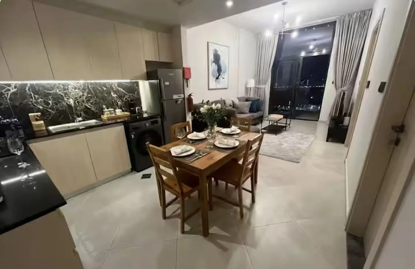 Open-concept apartment with a wooden dining table set for four, a modern kitchen, and a living area with a city view.