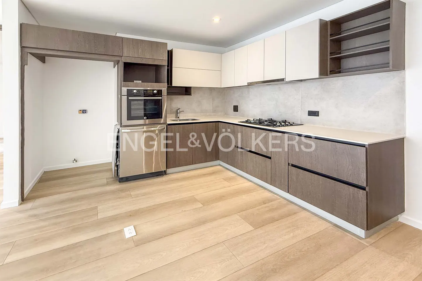 A modern kitchen with light wood floors, two-tone cabinets, stainless steel appliances, and a gas cooktop.