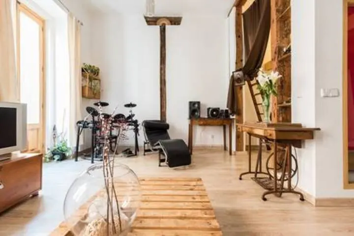 Bright living room with a wooden pallet coffee table, black lounge chair, drum set, and a vintage sewing machine desk.