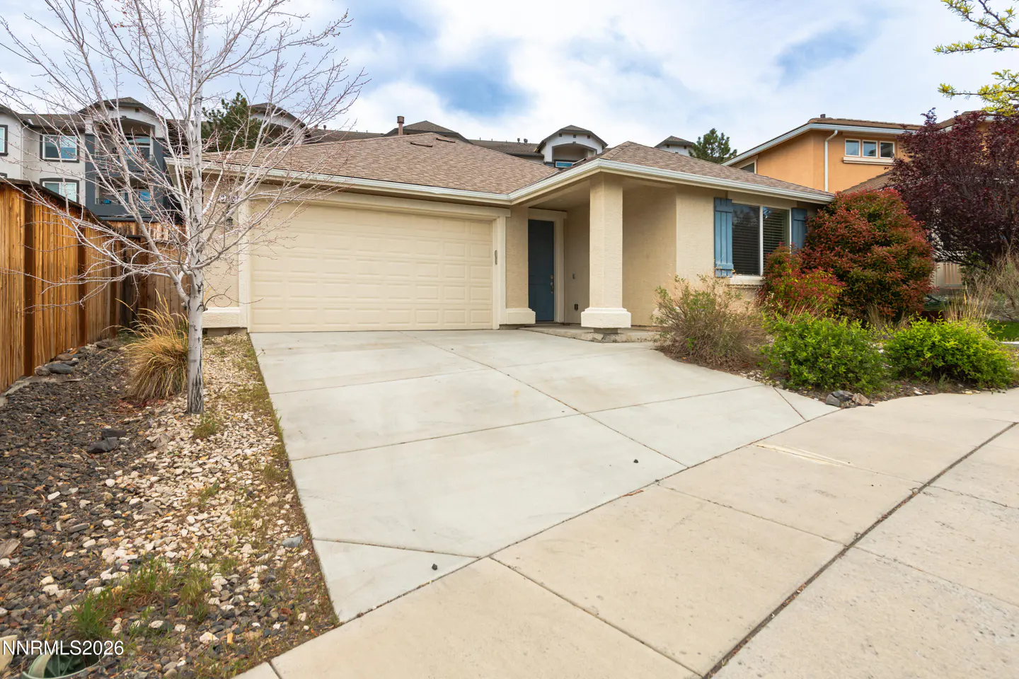 Beige single-story house with a two-car garage, blue door, and blue shutters. A concrete driveway leads to the street.