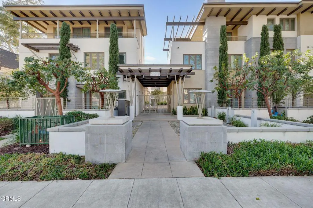 Exterior view of a modern, multi-story apartment complex with a gated entrance and manicured landscaping.