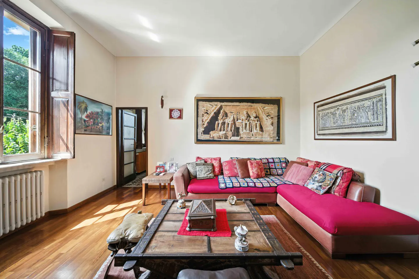 Living room with hardwood floors, a red sectional sofa, and a large wooden coffee table. Art adorns the walls.