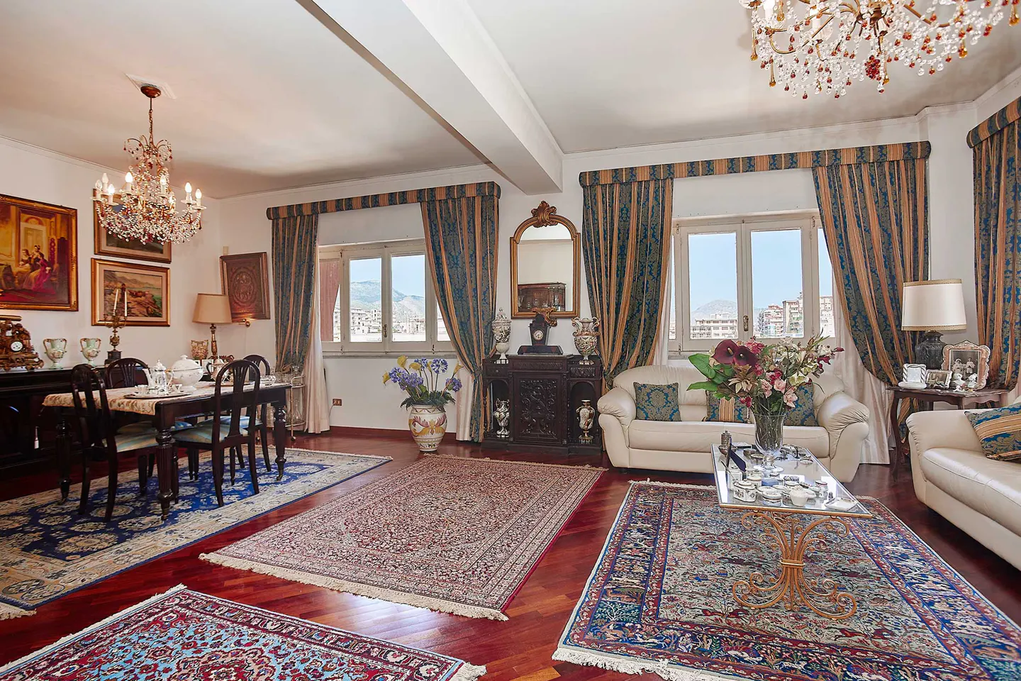 A spacious living and dining area with hardwood floors, rugs, sofas, and a chandelier.