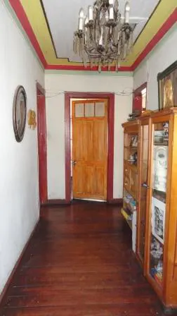 Hallway with wood floors, white walls, and a chandelier. A wooden door is centered, flanked by a cabinet on the right. The ceiling has red and yellow trim.