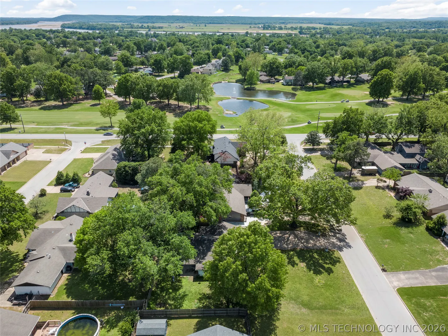 Aerial view of a residential neighborhood with green lawns, mature trees, and a golf course with ponds in the background.