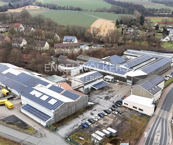 Aerial view of commercial buildings with solar panels, parking lot, and rural background.