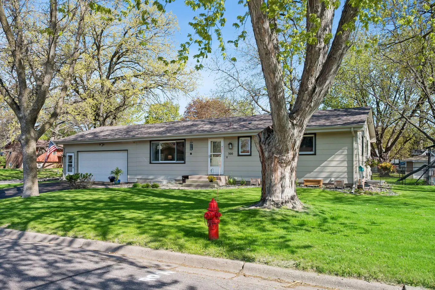 Beige ranch-style house with a white garage door, green trim, and a red fire hydrant in the front yard.