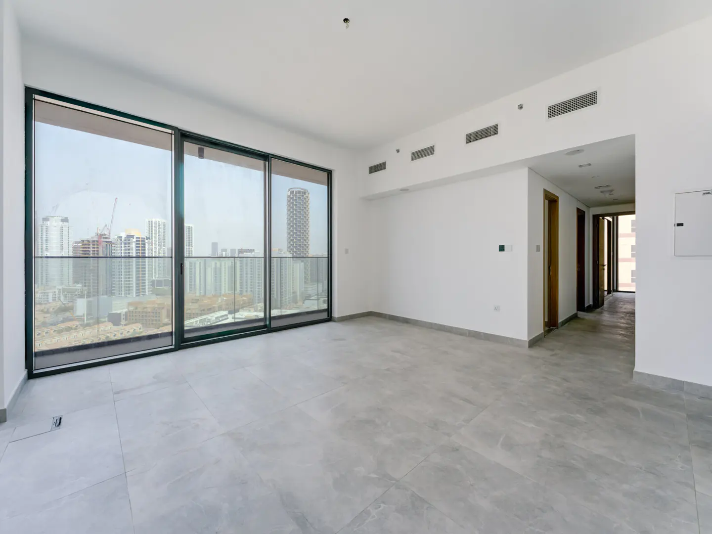 Empty, bright room with gray tile floor, white walls, and large sliding glass doors to a city view.
