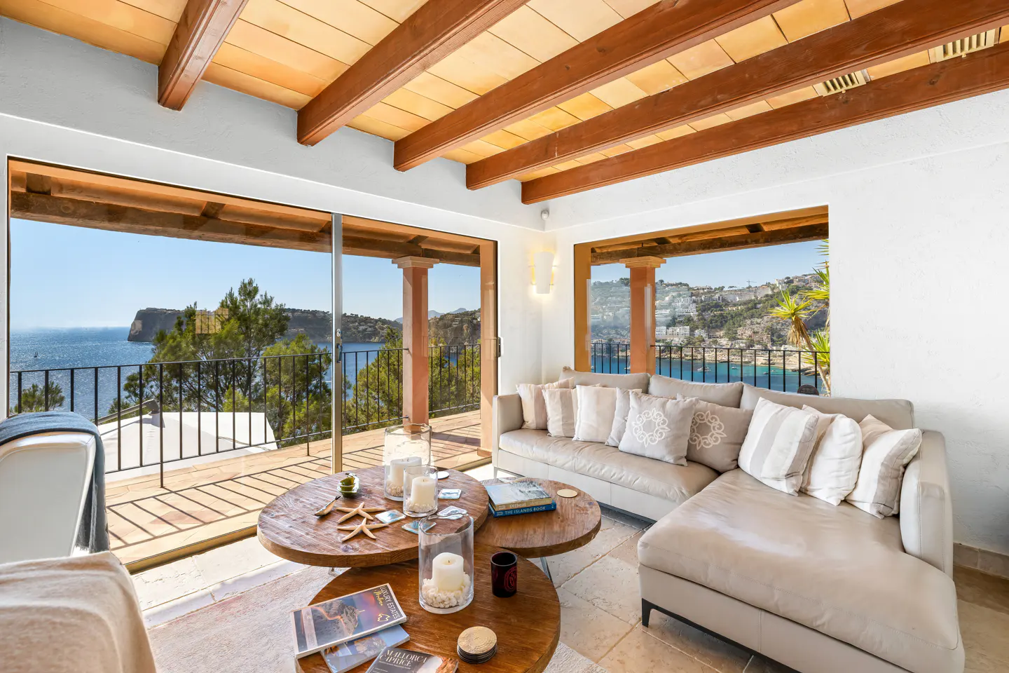 Living room with a beige sectional sofa, two round wooden coffee tables, and large windows overlooking the ocean.