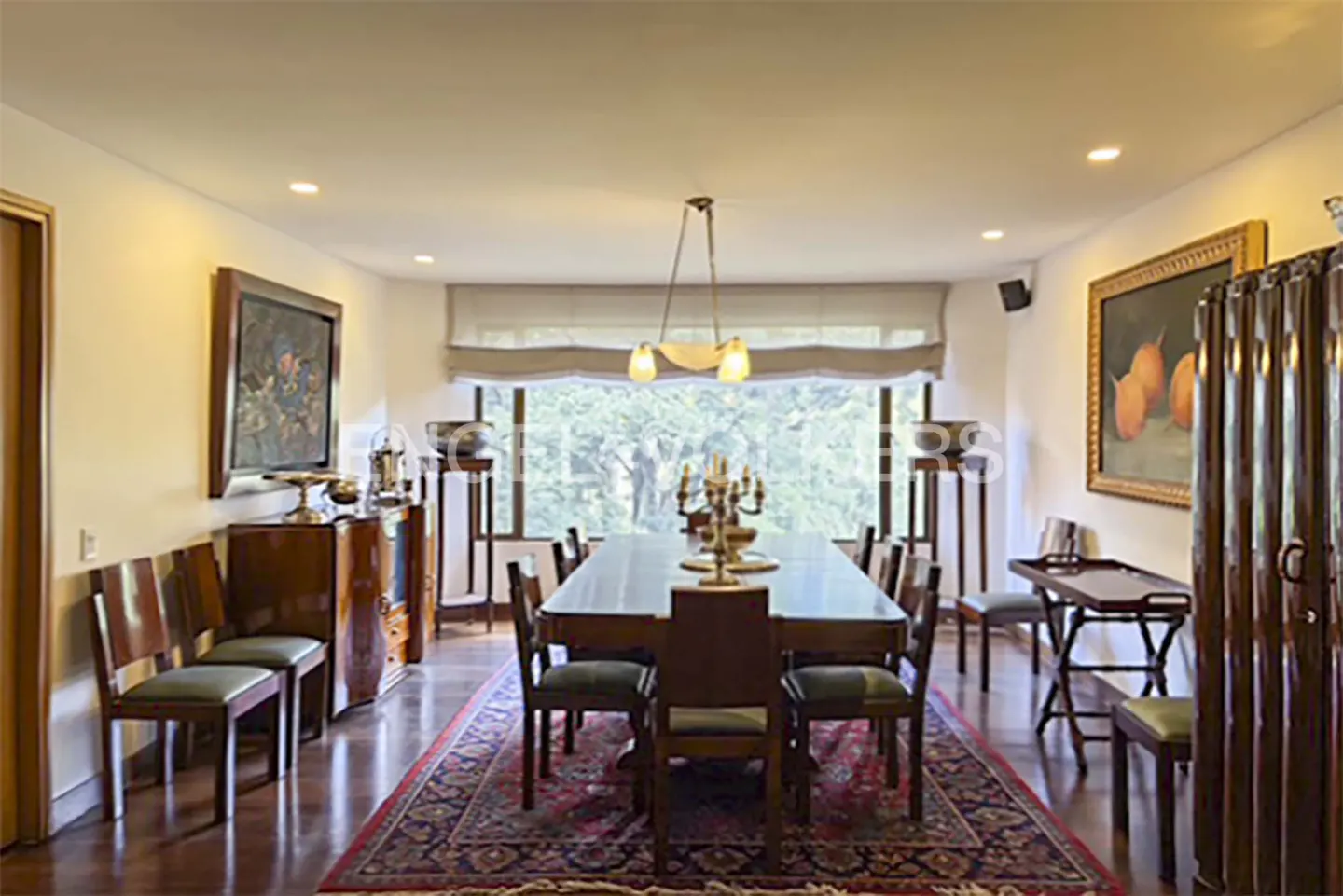 Formal dining room with a long wooden table, green-cushioned chairs, a red patterned rug, and large framed wall art.