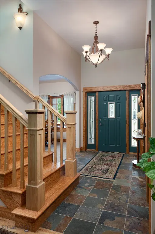 A home's foyer with a teal front door, wood trim, and a patterned rug on a slate tile floor. A staircase is on the left.