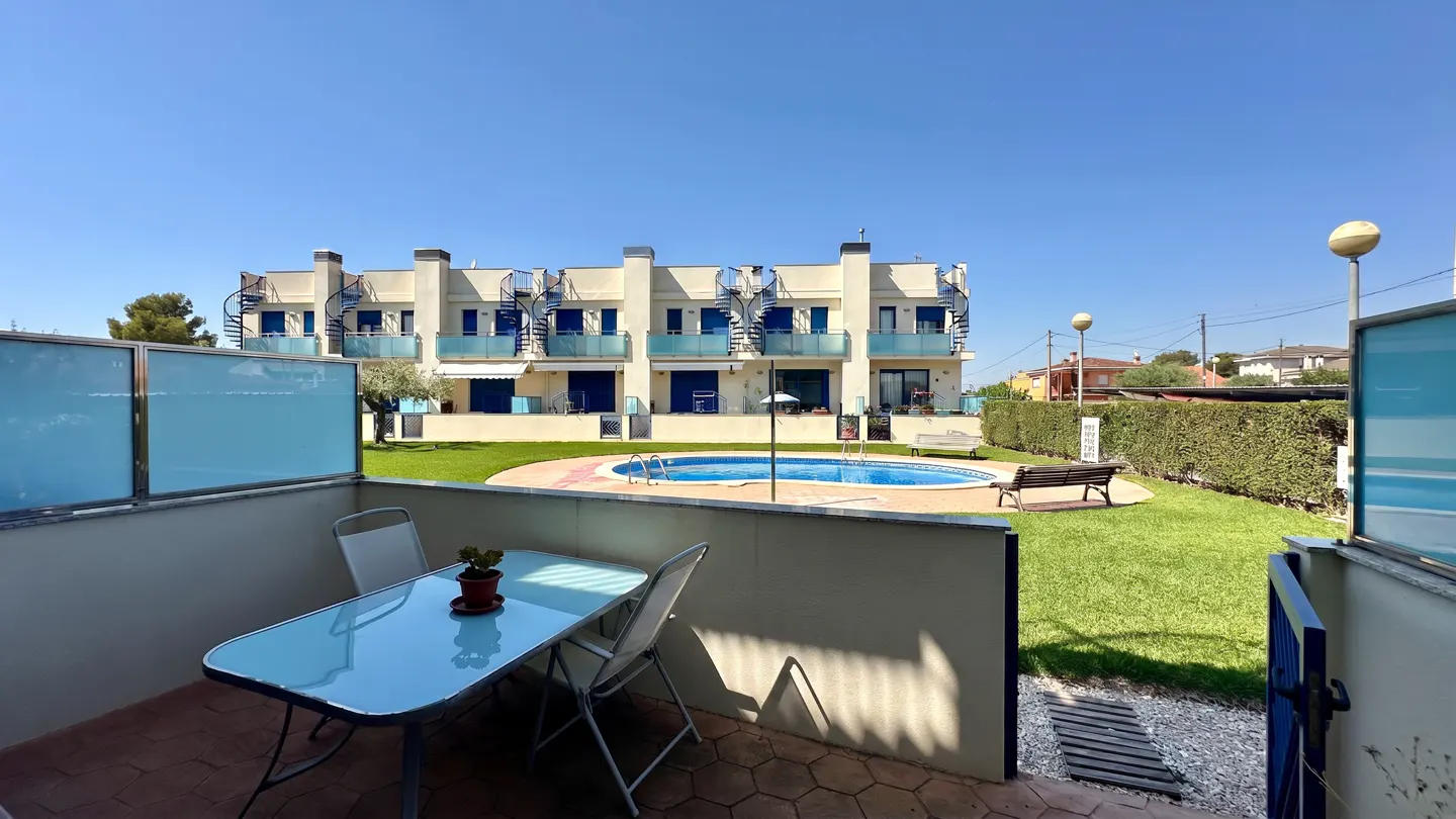 View from a patio with a blue table and chairs, overlooking a pool and apartments with blue accents.