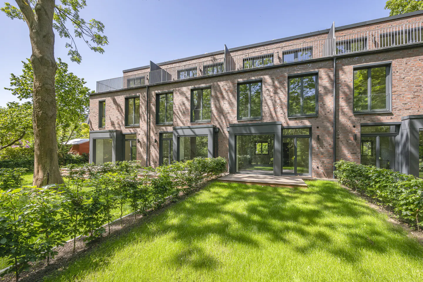 Exterior view of a three-story brick townhouse with large windows and a green lawn.