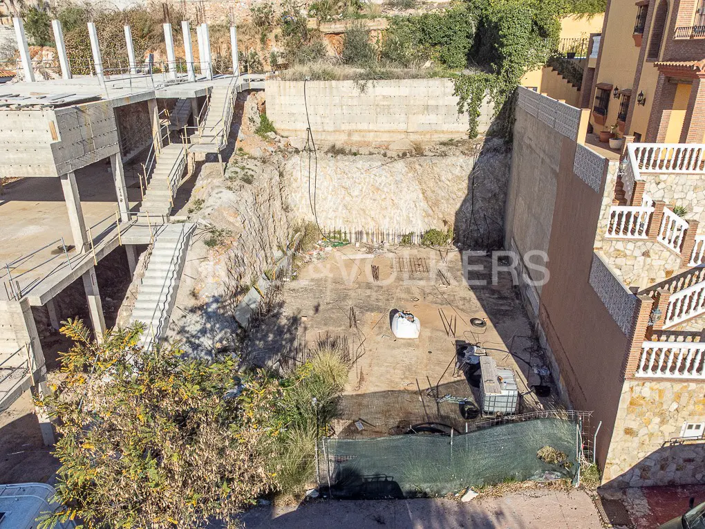 Aerial view of a construction site with a concrete foundation, retaining walls, and a partially built structure with stairs.