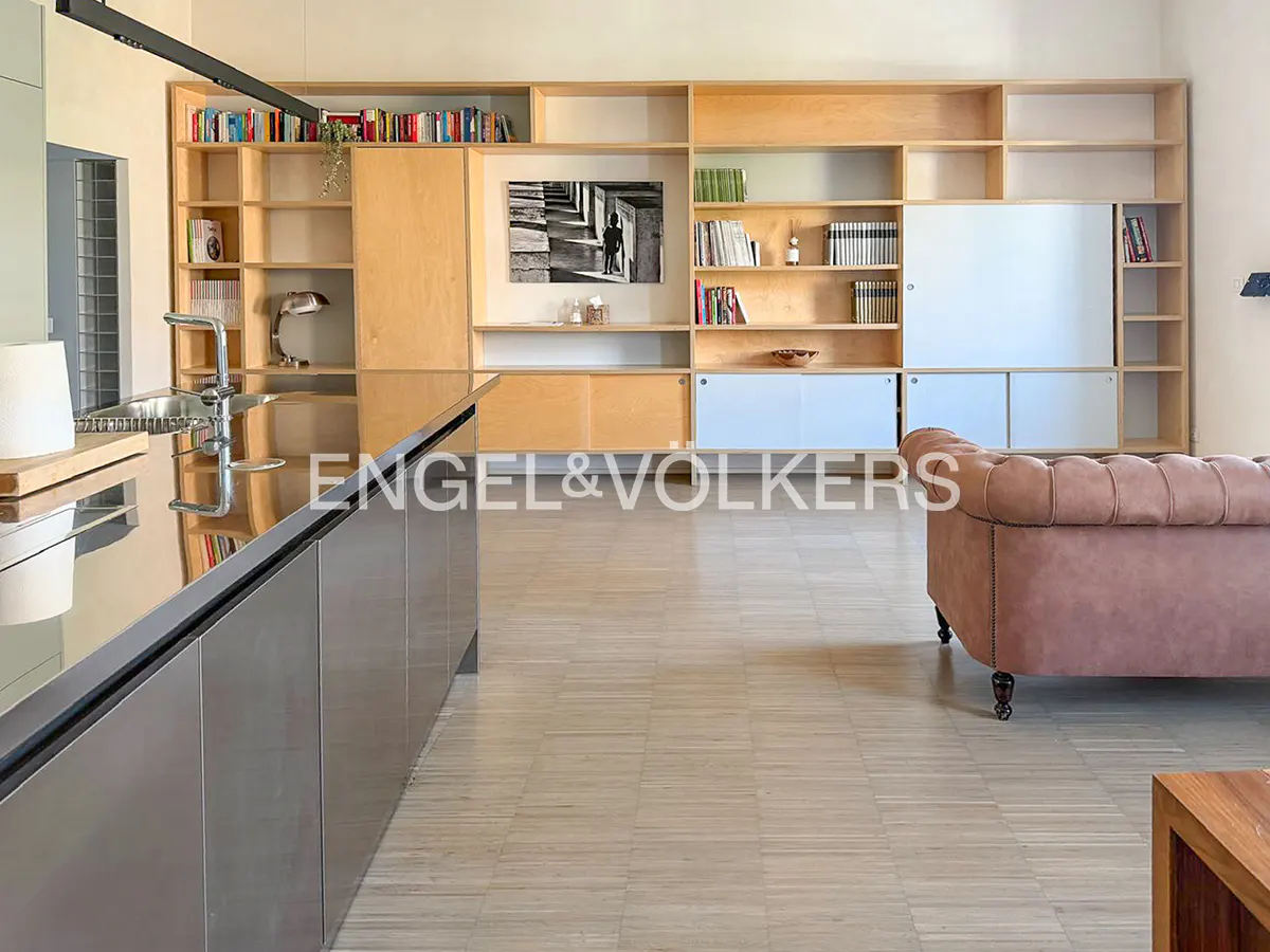 A modern apartment interior with a kitchen island, a large wooden bookshelf, and a pink sofa.