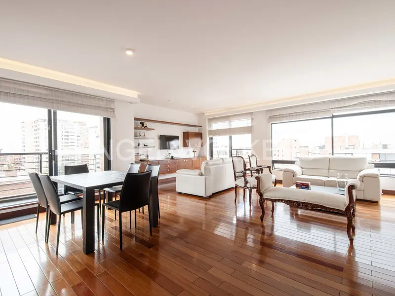 Bright, open-concept living and dining area with hardwood floors. White sofas and chairs face large windows with city views. Black dining table with chairs.