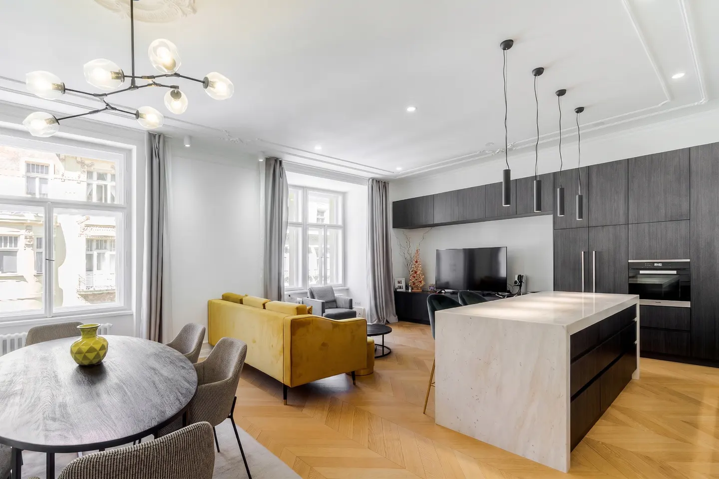 Modern open-plan living area with a yellow sofa, round dining table, and a kitchen island with dark wood cabinets.