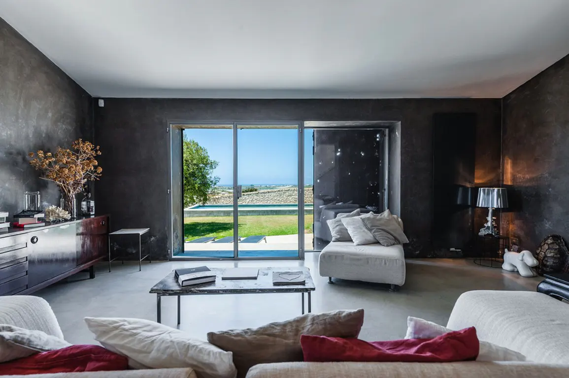 Modern living room with gray walls, a dark wood sideboard, and a sliding glass door to a green lawn and pool.