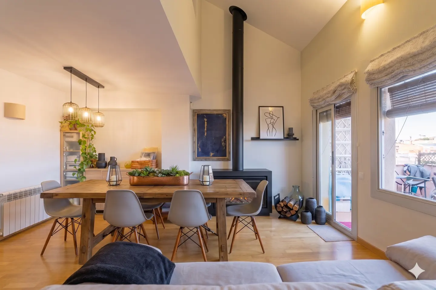 Bright, modern living room with a wood dining table, gray chairs, and a black fireplace. Balcony access with blinds and a view.