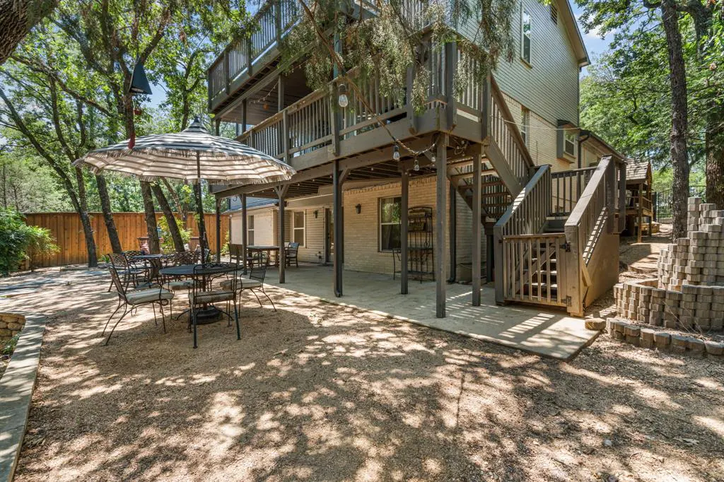 Backyard patio with outdoor seating under a striped umbrella, a two-story deck, and a staircase leading to the upper level.