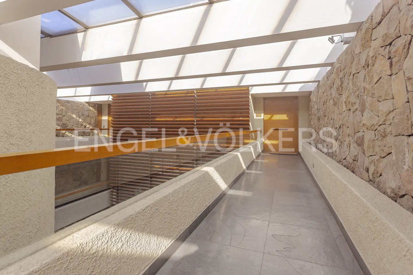 Interior view of a modern hallway with stone walls, a skylight, and a wooden railing.
